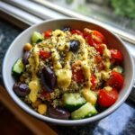 Close-up of a Mediterranean Quinoa Bowl featuring quinoa, tomatoes, cucumbers, olives, and a generous drizzle of lemon tahini sauce.