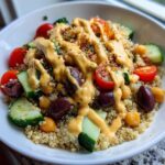 A vibrant Mediterranean Quinoa Bowl featuring quinoa, cucumbers, tomatoes, olives, chickpeas, and a generous drizzle of lemon tahini sauce.
