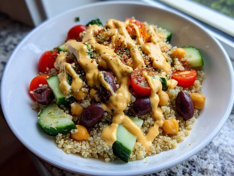 A vibrant Mediterranean Quinoa Bowl featuring quinoa, cucumbers, tomatoes, olives, chickpeas, and a generous drizzle of lemon tahini sauce.
