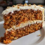 A thick slice of Moist Carrot Cake with Cream Cheese Frosting, showing two cake layers and nuts on top.
