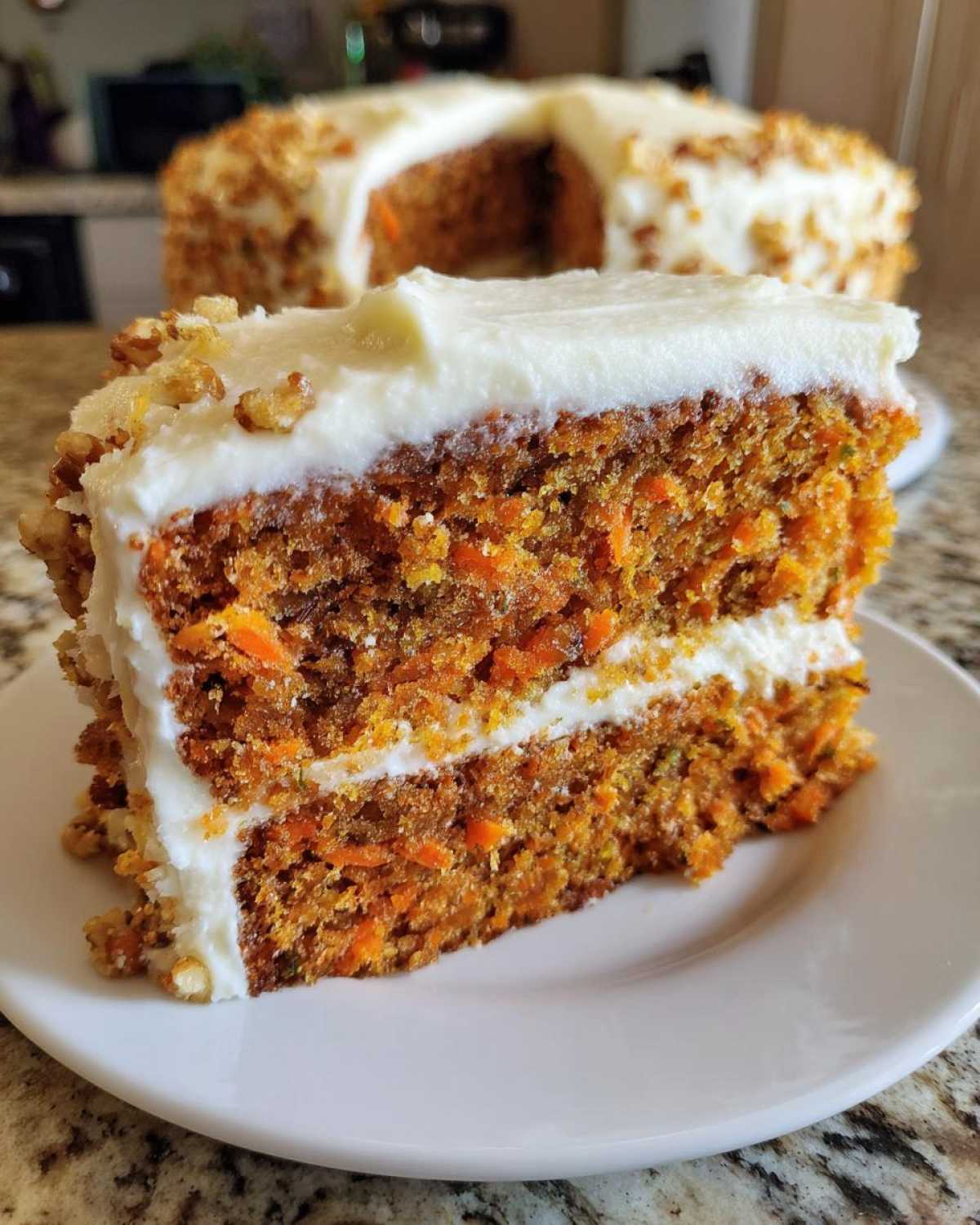 A thick slice of Moist Carrot Cake with Cream Cheese Frosting showing visible shredded carrots and chopped nuts.