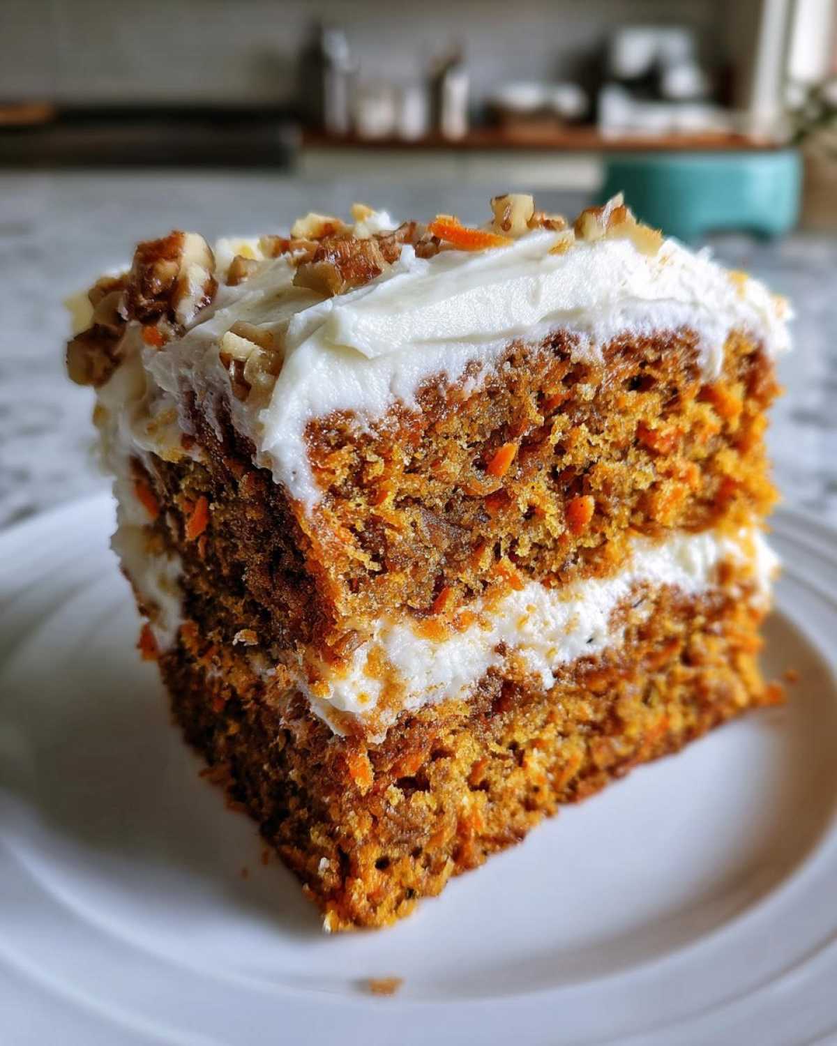 A close-up of a thick slice of Moist Carrot Cake with Cream Cheese Frosting, topped with walnuts.