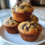 A stack of four moist Chocolate Chip Banana Muffins with golden brown tops covered in melted chocolate chips.