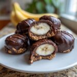 A stack of No-Bake Chocolate Covered Banana Bites, one cut open revealing a banana slice center.