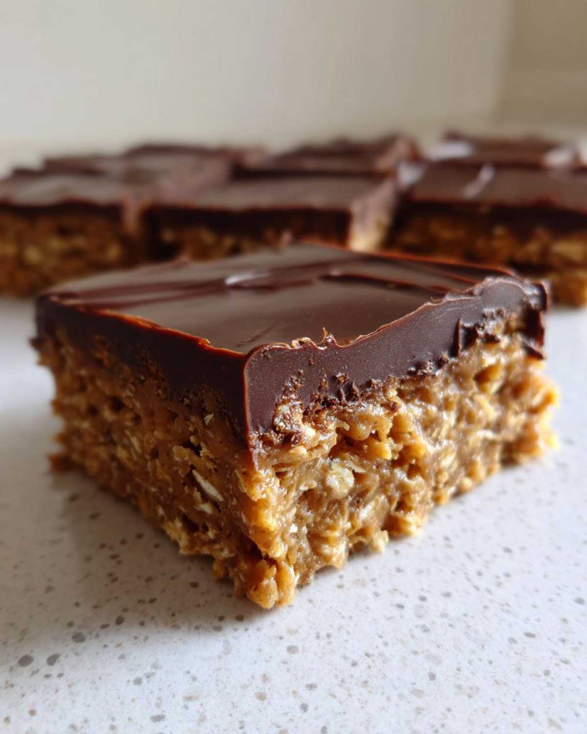 A close-up of one No-Bake Chocolate Peanut Butter Oat Bar showing the thick peanut butter oat base and smooth chocolate topping.