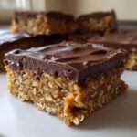 A close-up of a single square of No-Bake Chocolate Peanut Butter Oat Bars showing the thick oat base and smooth chocolate topping.