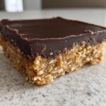 A single square of No-Bake Chocolate Peanut Butter Oat Bars showing the thick peanut butter oat base and smooth chocolate topping.