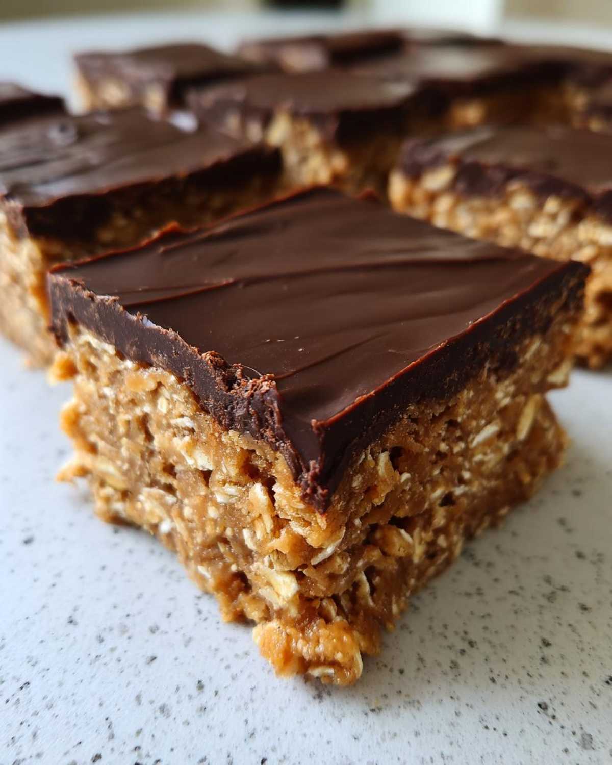 A close-up of a square No-Bake Chocolate Peanut Butter Oat Bars piece showing the thick oat base and chocolate topping.