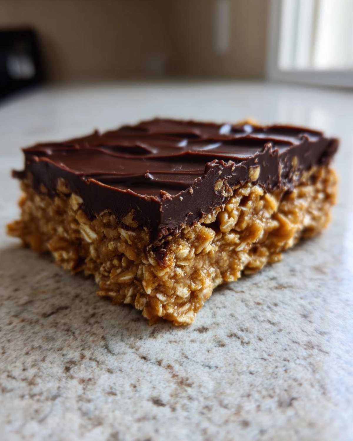 A close-up of a square No-Bake Chocolate Peanut Butter Oat Bars with a thick chocolate topping.