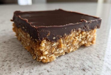 A single square of No-Bake Chocolate Peanut Butter Oat Bars showing the thick peanut butter oat base and smooth chocolate topping.