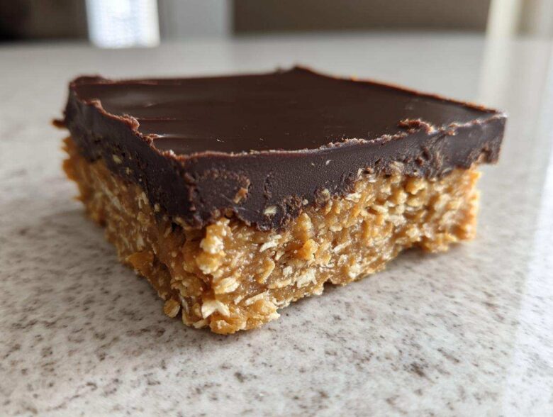 A single square of No-Bake Chocolate Peanut Butter Oat Bars showing the thick peanut butter oat base and smooth chocolate topping.