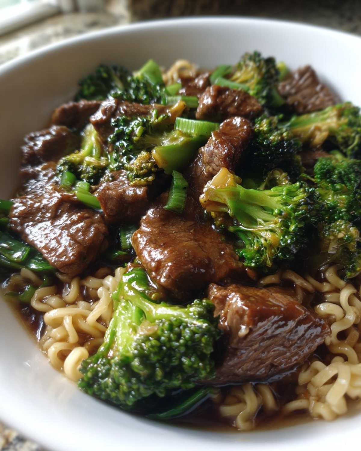 A close-up view of a white bowl filled with One-Pot Beef and Broccoli Ramen Noodles, featuring tender beef chunks and bright green broccoli florets.