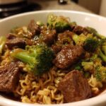 Close-up of a white bowl filled with One-Pot Beef and Broccoli Ramen Noodles, featuring savory beef chunks and bright green broccoli florets.
