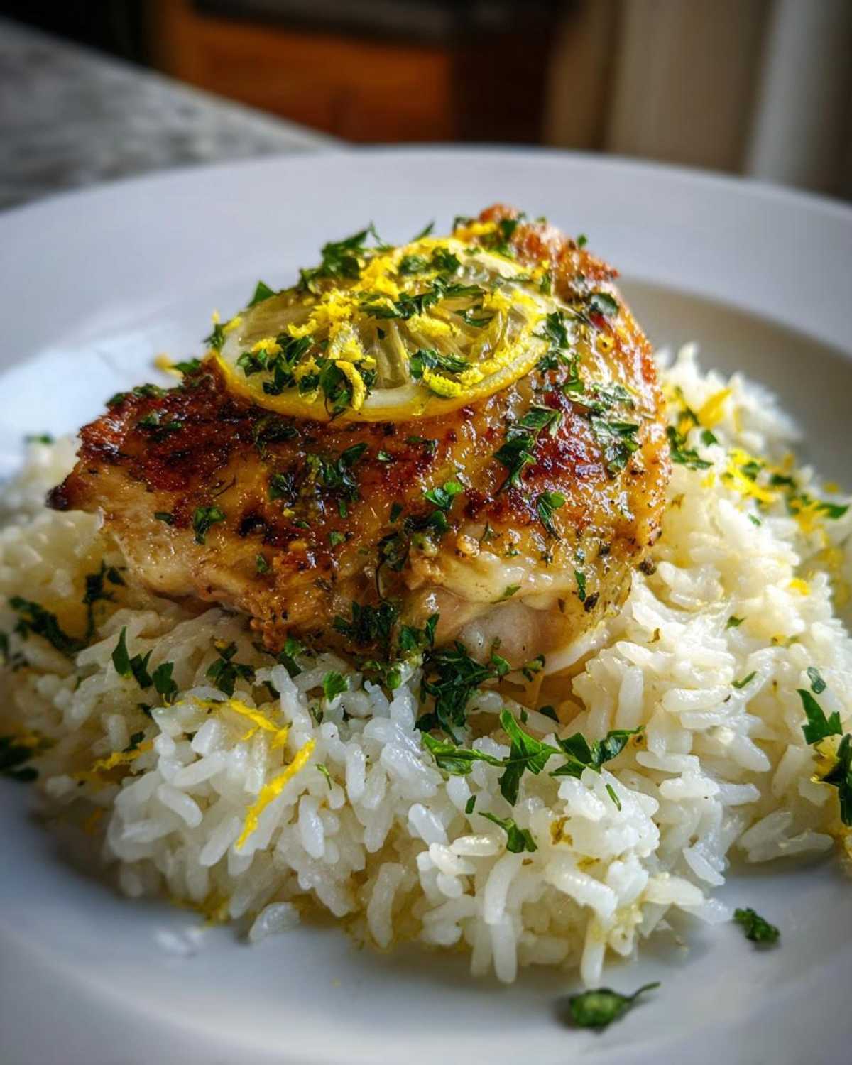 Close-up of a perfectly cooked chicken breast served over fluffy white rice, garnished with lemon slice and fresh herbs for One-Pot Chicken and Rice with Lemon and Herbs.