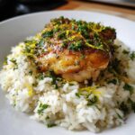 A serving of fluffy white rice topped with a golden-brown chicken thigh, garnished heavily with fresh parsley and lemon zest for One-Pot Chicken and Rice with Lemon and Herbs.