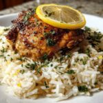 A perfectly cooked piece of chicken served over fluffy white rice, garnished with herbs and a lemon slice for One-Pot Chicken and Rice with Lemon and Herbs.