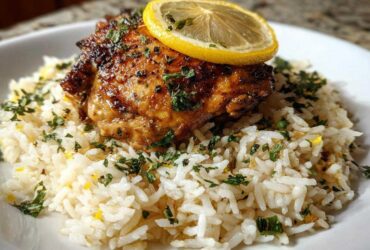 A perfectly cooked piece of chicken served over fluffy white rice, garnished with herbs and a lemon slice for One-Pot Chicken and Rice with Lemon and Herbs.