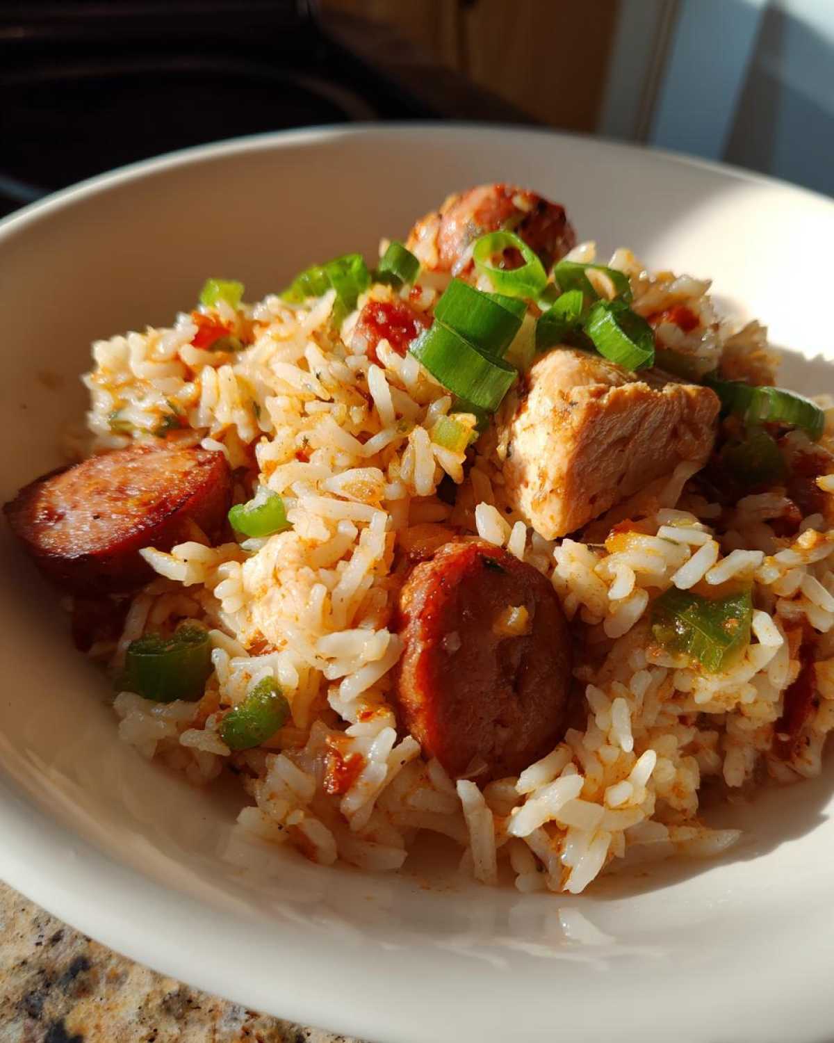 A close-up of a bowl filled with One-Pot Chicken Jambalaya, featuring rice, chicken chunks, sliced sausage, and green onions.