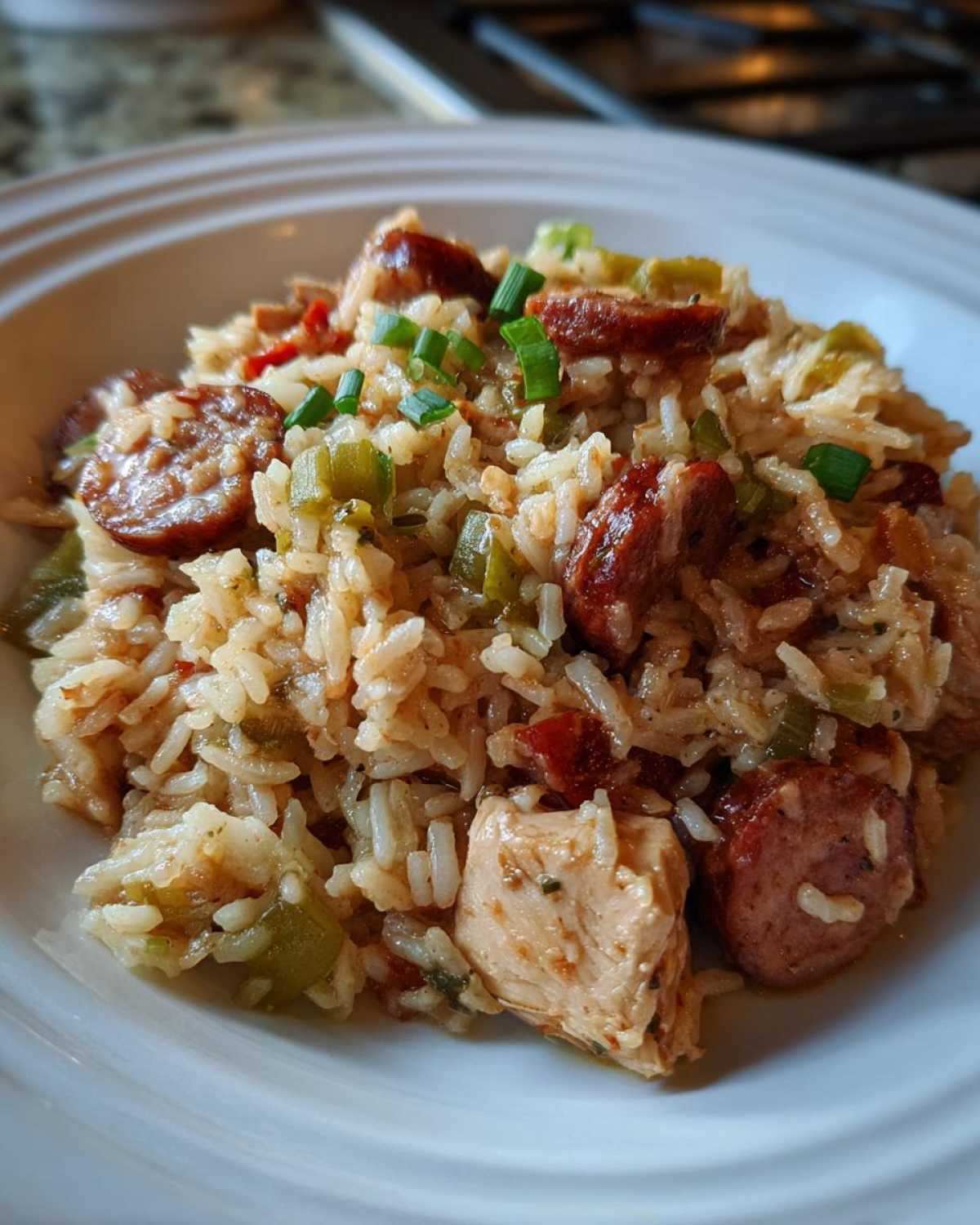 Close-up of a white bowl filled with One-Pot Chicken Jambalaya featuring rice, sausage slices, chicken chunks, and green onions.