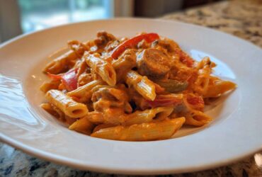 A close-up of a white bowl filled with One-Pot Creamy Cajun Sausage Pasta, featuring penne, sausage slices, and peppers.