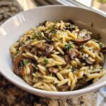 Close-up of One-Pot Creamy Mushroom Orzo garnished with fresh thyme sprigs in a white bowl.