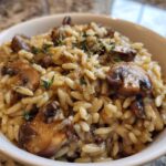 A close-up of a white bowl filled with One-Pot Creamy Mushroom Orzo, topped with sautéed mushrooms and thyme.