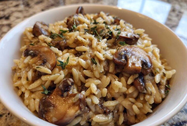 A close-up of a white bowl filled with One-Pot Creamy Mushroom Orzo, topped with sautéed mushrooms and thyme.