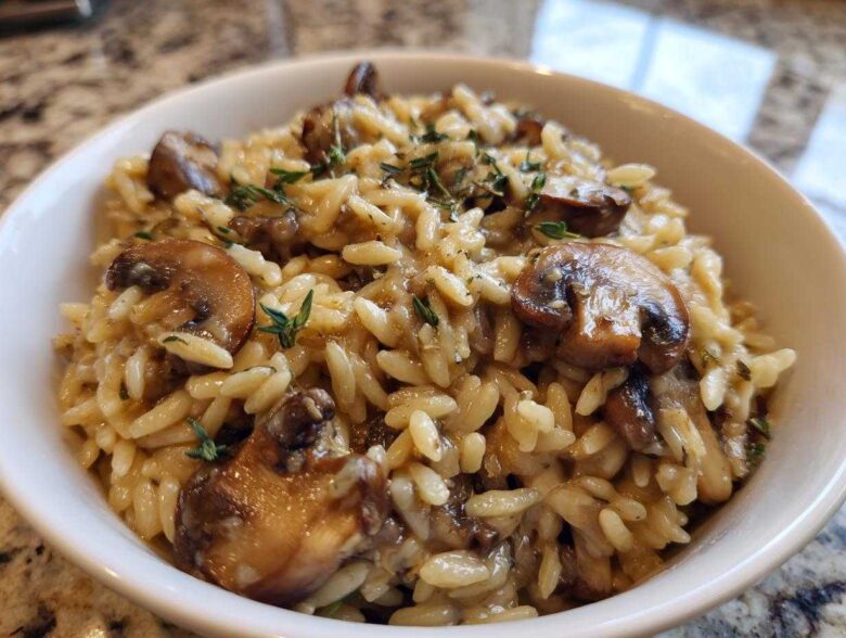 A close-up of a white bowl filled with One-Pot Creamy Mushroom Orzo, topped with sautéed mushrooms and thyme.