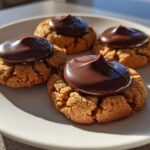 Four classic Peanut Butter Blossom Cookies with a dollop of melted chocolate frosting on a white plate.