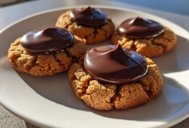 Four classic Peanut Butter Blossom Cookies with a dollop of melted chocolate frosting on a white plate.