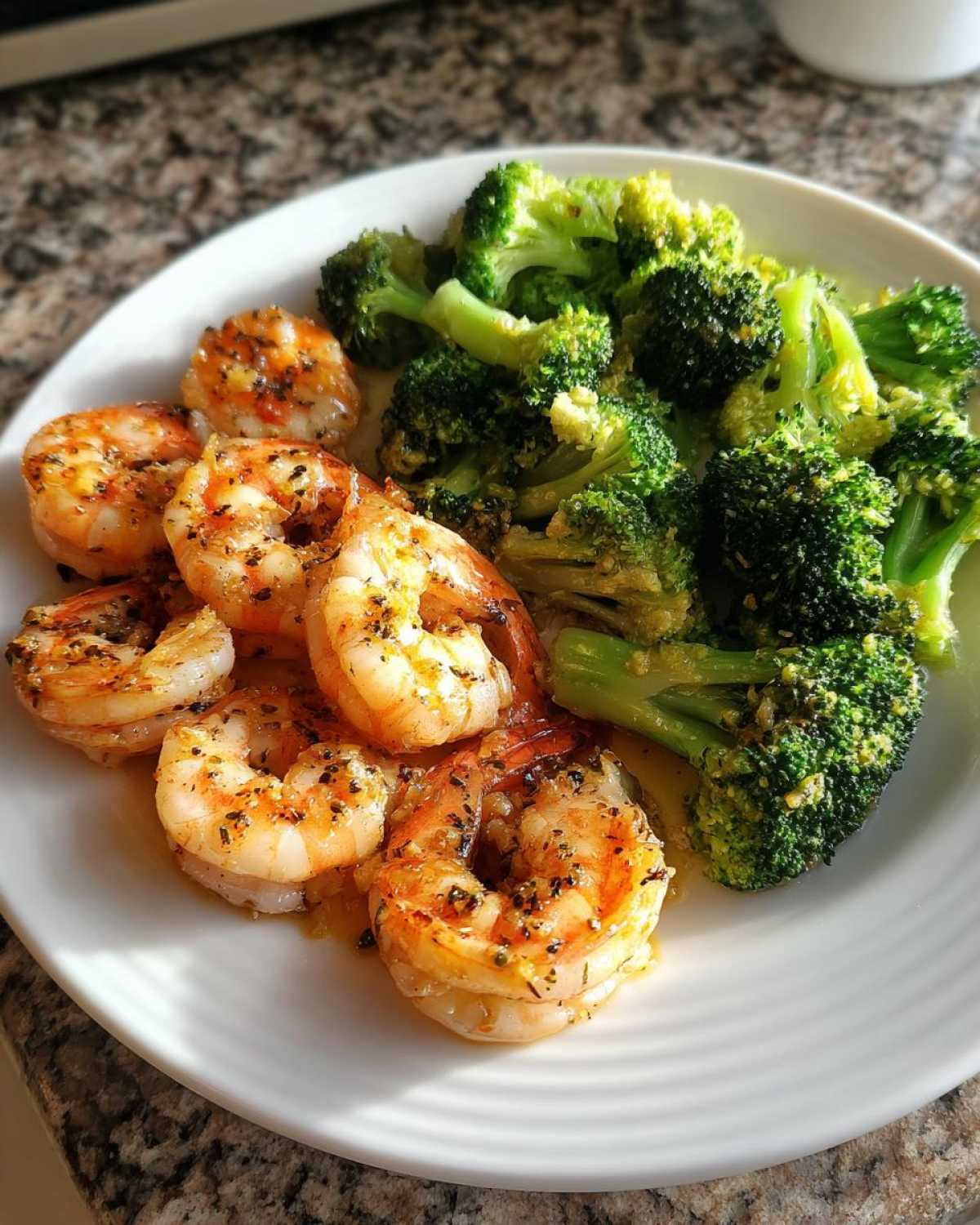 A white plate holding cooked shrimp seasoned with herbs next to bright green broccoli florets, representing Sheet Pan Garlic Butter Shrimp and Broccoli.