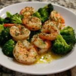 Close-up of cooked shrimp and bright green broccoli florets coated in garlic butter sauce.