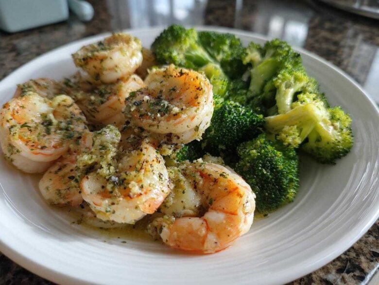 A white plate featuring cooked shrimp generously coated in garlic butter sauce next to bright green broccoli florets.