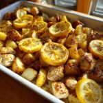 Close-up of Sheet Pan Lemon Pepper Chicken and Potatoes with roasted lemon slices in a white baking dish.