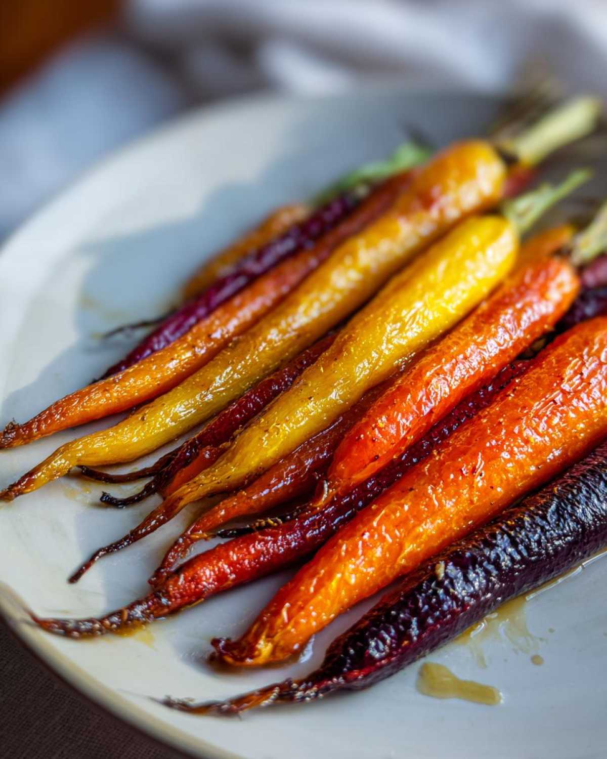 Close-up of glistening Sheet Pan Roasted Rainbow Carrots with Honey, showing orange, yellow, and purple varieties on a white plate.