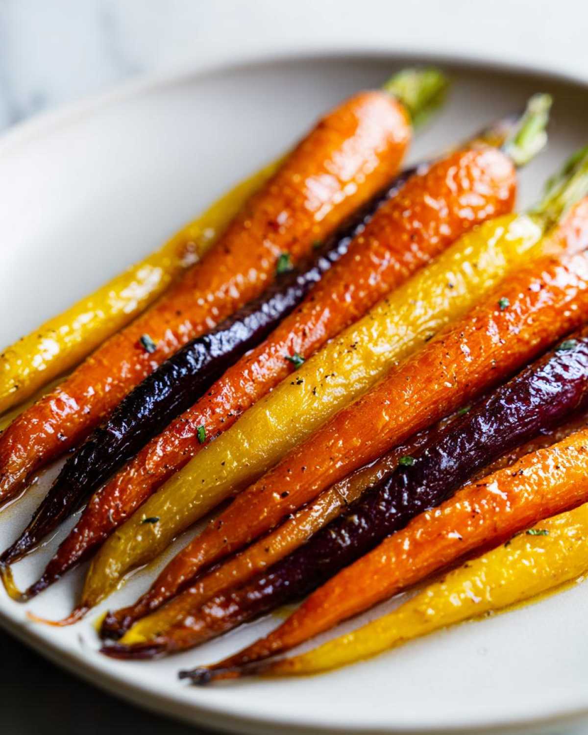 Close-up of glossy, glazed Sheet Pan Roasted Rainbow Carrots with Honey served on a white plate.