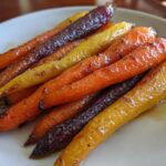 Close-up of glossy, roasted rainbow carrots glazed with honey, served on a white plate.