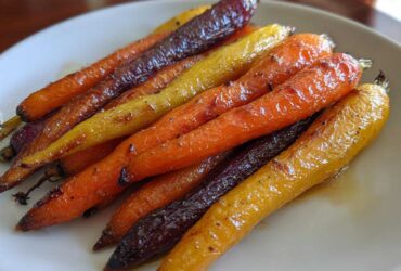 Close-up of glossy, roasted rainbow carrots glazed with honey, served on a white plate.