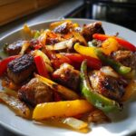 A close-up serving of Sheet Pan Sausage and Peppers featuring browned sausage chunks mixed with caramelized bell peppers and onions.