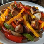 Close-up of cooked Sheet Pan Sausage and Peppers, featuring browned sausage chunks and roasted red, yellow, and green bell peppers.