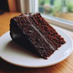 A moist slice of dark, rich Gluten-Free Chocolate Cake resting on a white plate.