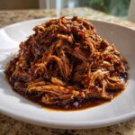 A generous mound of saucy Slow Cooker Honey Garlic Pulled Pork piled high on a white plate.