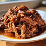 A pile of shredded, saucy Slow Cooker Honey Garlic Pulled Pork glistening on a white plate.