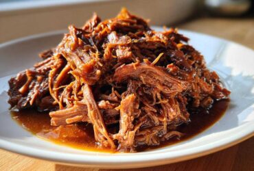 A pile of shredded, saucy Slow Cooker Honey Garlic Pulled Pork glistening on a white plate.