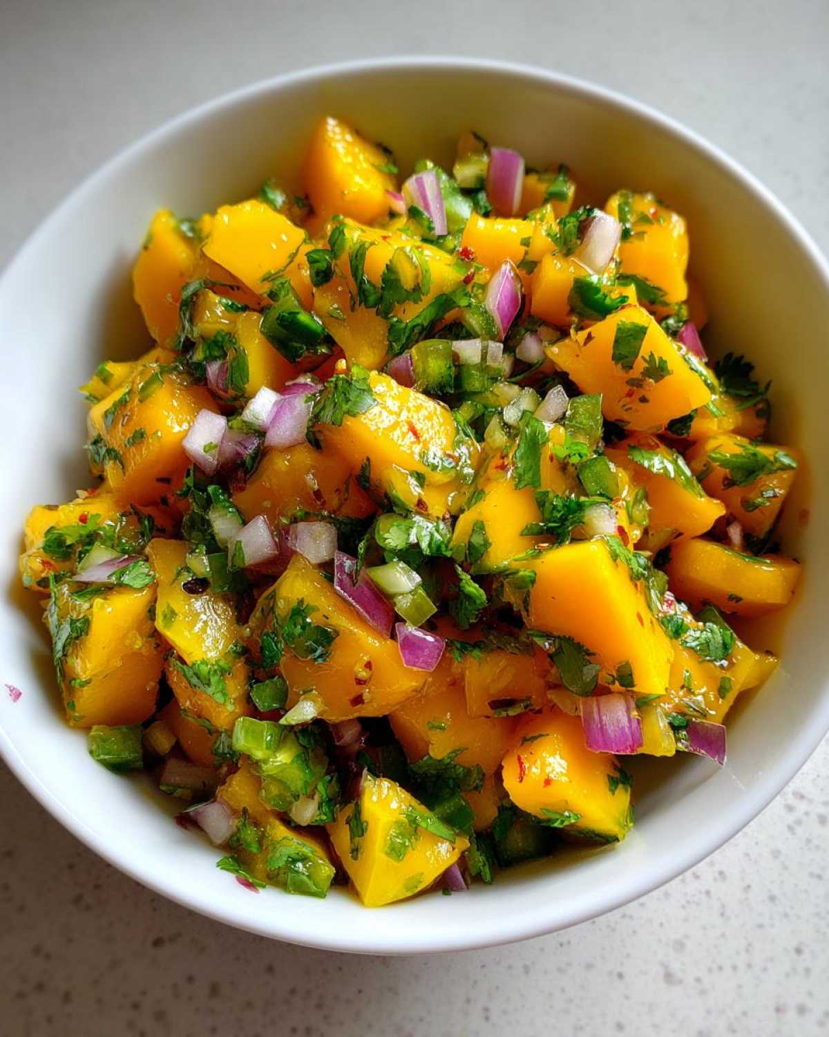 Close-up of vibrant, freshly made Spicy Mango Salsa with diced mango, red onion, and cilantro in a white bowl.