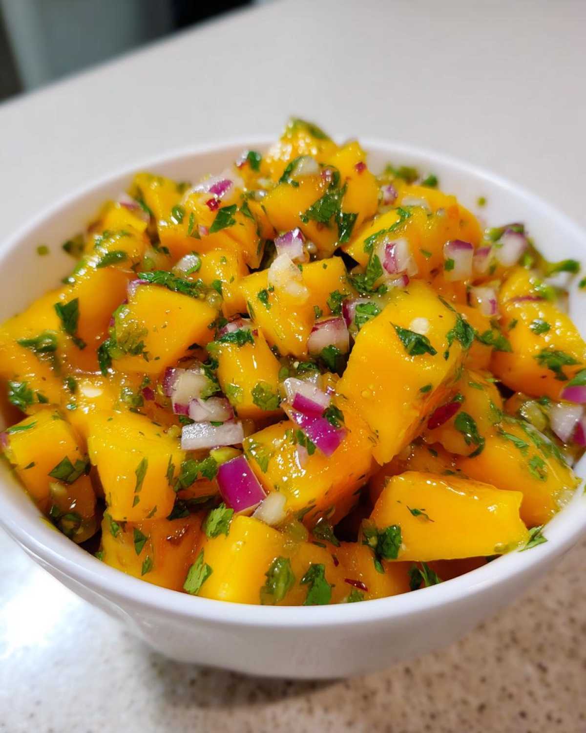Close-up of bright yellow mango chunks mixed with red onion and cilantro in a Spicy Mango Salsa.