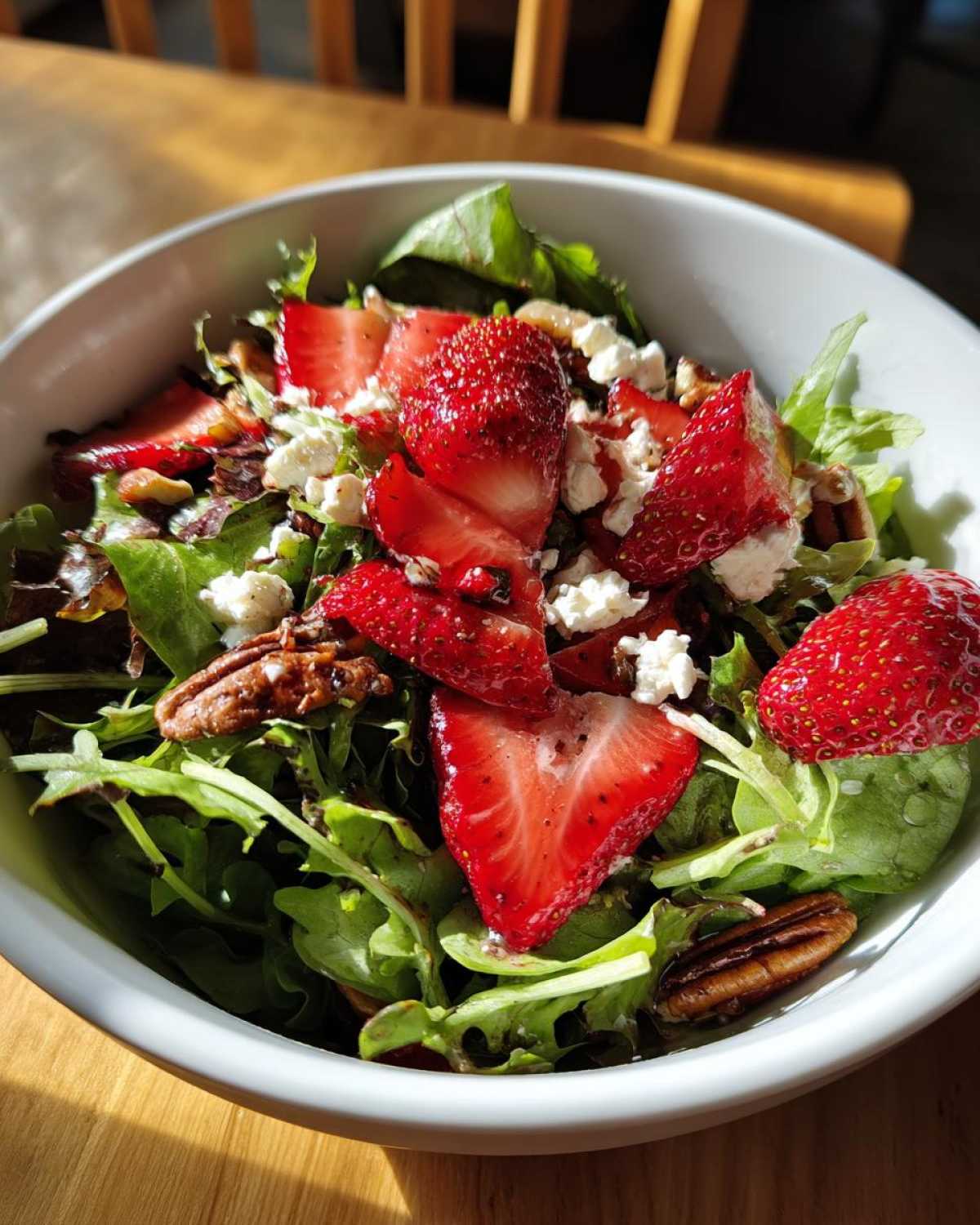 A vibrant bowl of Spring Mix Salad with Strawberries and Goat Cheese, topped with pecans and a light dressing.
