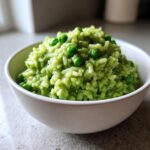 A close-up of creamy Spring Pea and Mint Risotto, topped with whole peas, served in a white bowl.