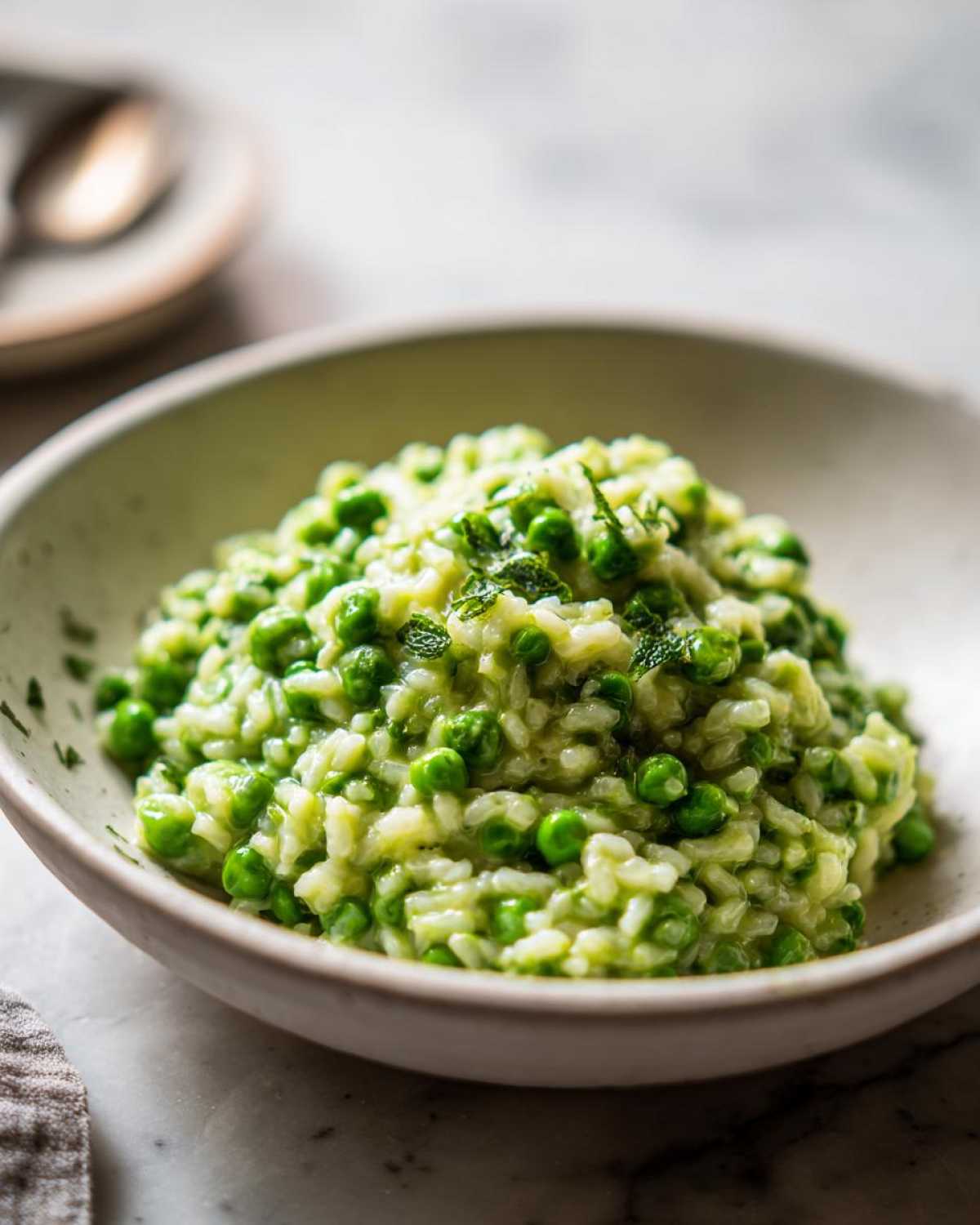 A close-up of creamy Spring Pea and Mint Risotto served in a light-colored bowl, topped with fresh mint.