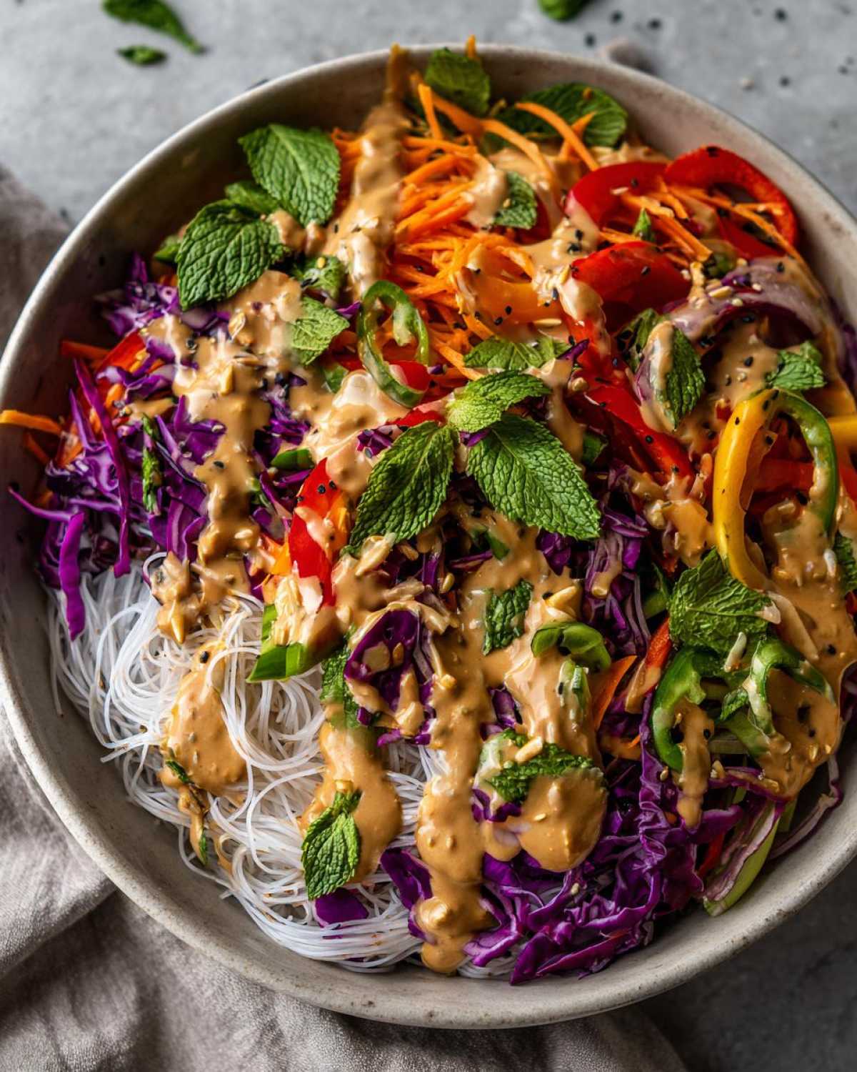Close-up of a colorful Spring Roll Bowl with Peanut Sauce, featuring rice noodles, shredded cabbage, carrots, peppers, and fresh mint.